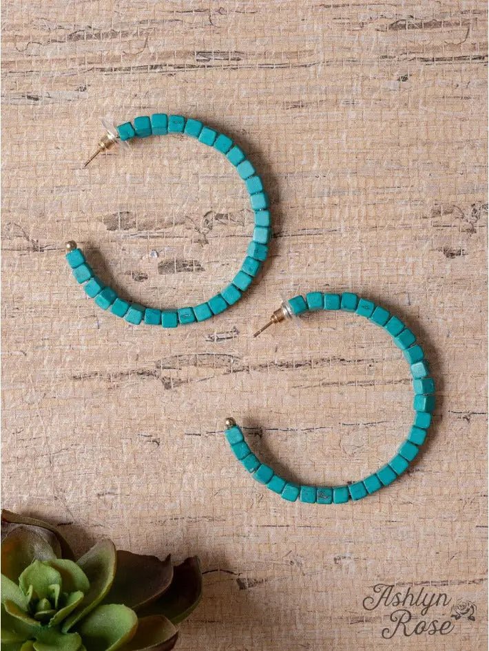 Flat lay of turquoise square beaded hoop earrings arranged on a natural background, showcasing their bold color and texture.