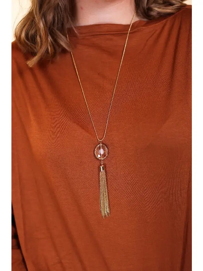 Woman wearing a rust-colored top with a long gold necklace featuring a faceted gemstone pendant and a cascading gold chain tassel.
