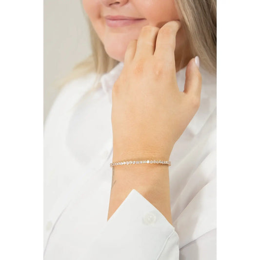 Close-up of a woman's wrist wearing the Starlight Whisper Bracelet — a delicate gold-toned chain adorned with small, sparkling crystals — styled with a white button-up shirt.