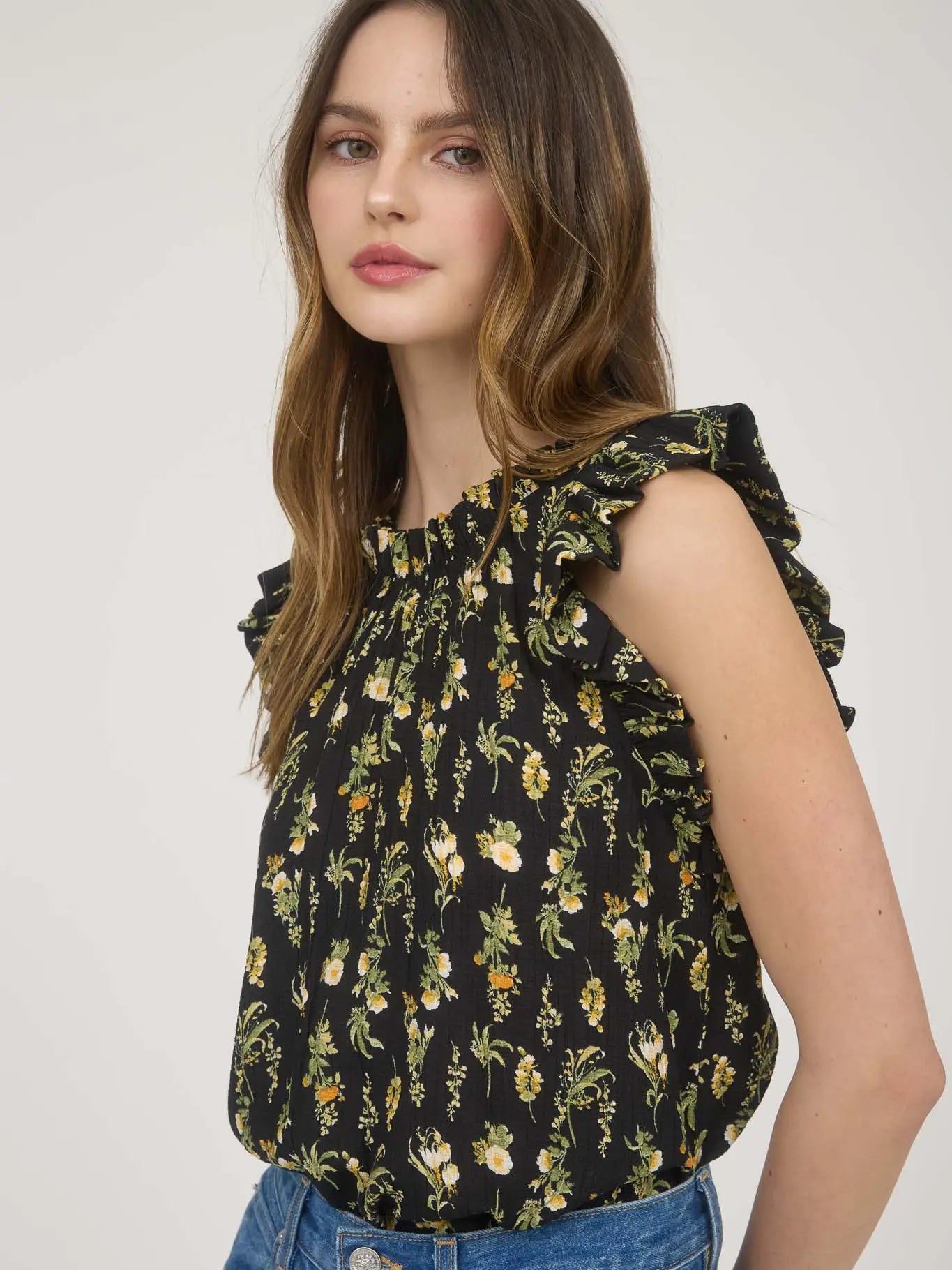 Women's sleeveless black woven blouse with yellow and white floral print, round neckline, ruffle sleeve detail, and back keyhole eye closure made from rayon-blend fabric