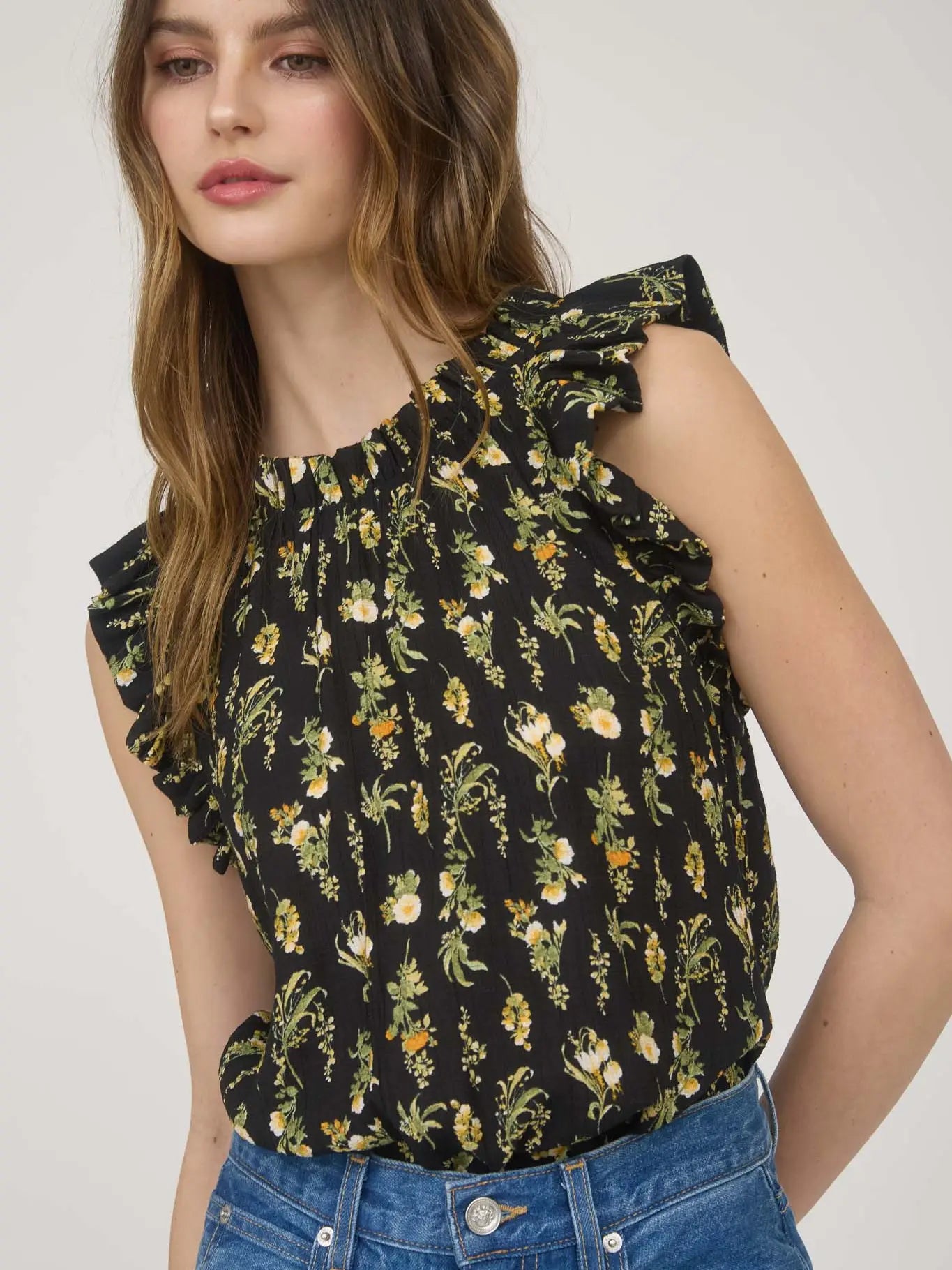 Women's sleeveless black woven blouse with yellow and white floral print, round neckline, ruffle sleeve detail, and back keyhole eye closure made from rayon-blend fabric