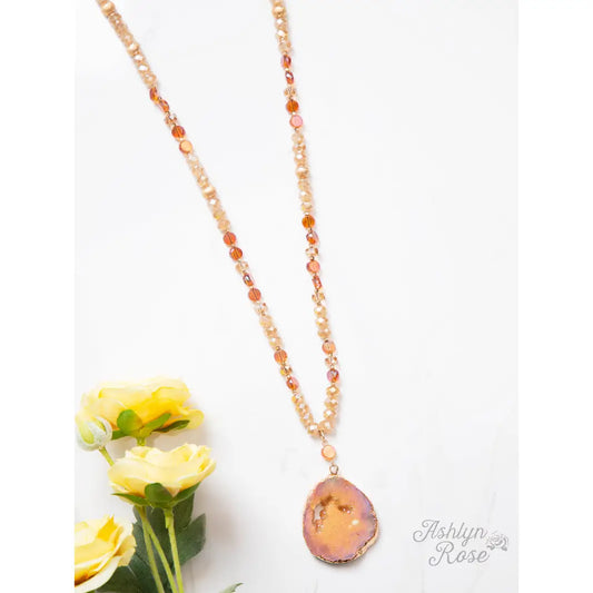 28-inch necklace with a 3-inch fabric pendant in warm sunset tones, displayed on a wood background.