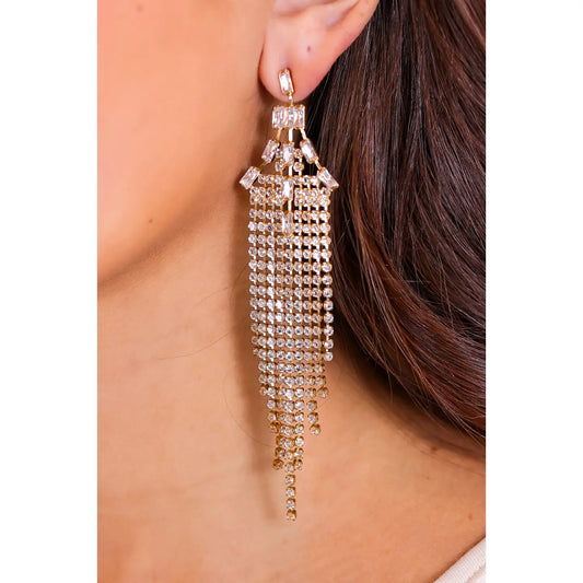 Close-up of a woman's ear wearing the Dazzle Drop Earrings — long, gold-toned chandelier earrings with cascading strands of crystal rhinestones.