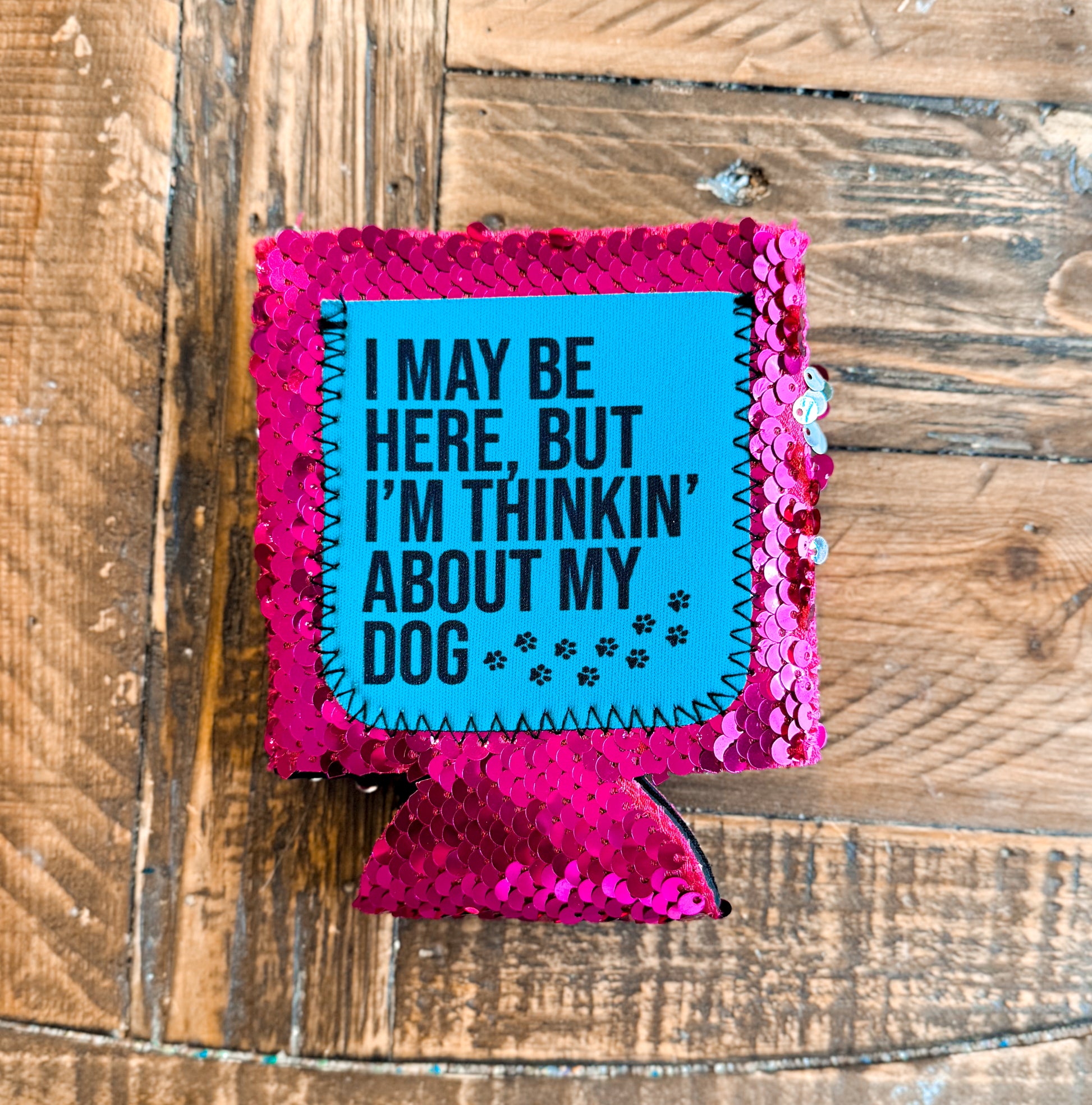 Hot pink sequin can cooler with a turquoise patch that says âI MAY BE HERE, BUT IâM THINKINâ ABOUT MY DOGâ with little paw prints.