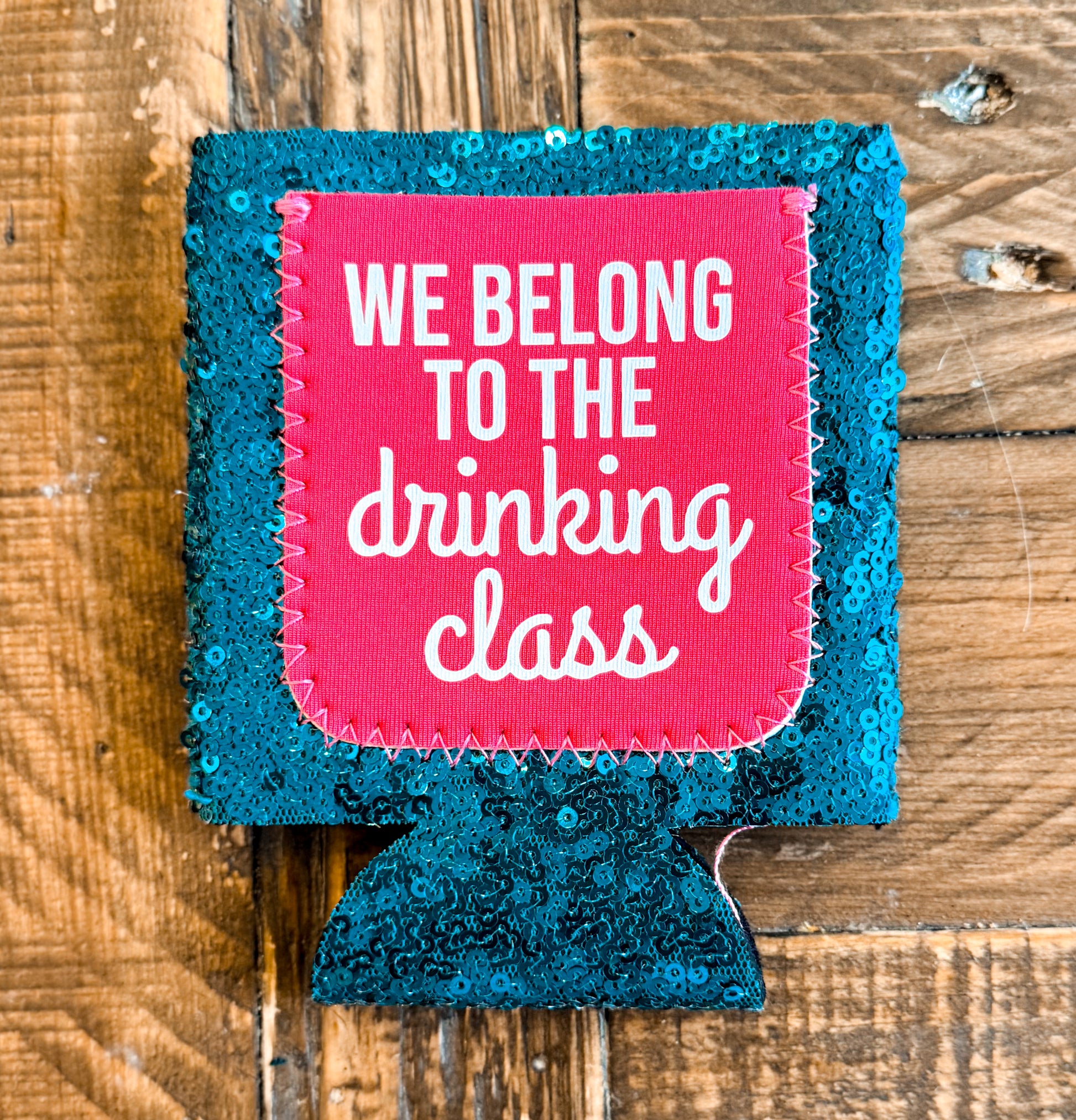 Teal sequin can cooler with a hot pink patch that reads âWE BELONG TO THE DRINKING CLASSâ in playful white text.