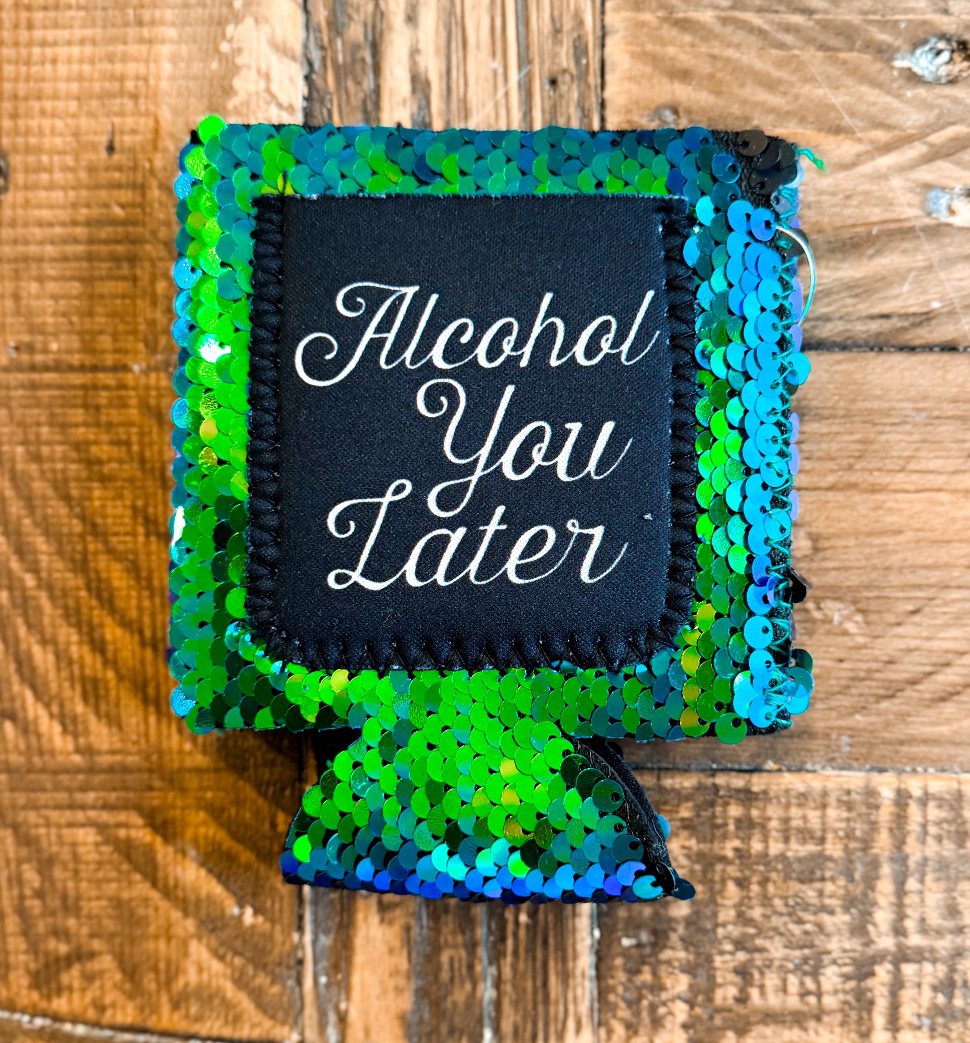 Green and blue sequin can cooler with a black patch that says âAlcohol You Laterâ in elegant white script.