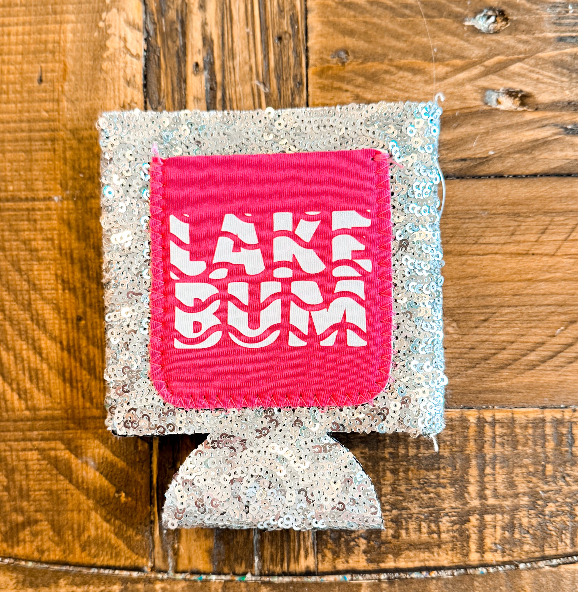 Silver sequin can cooler with a hot pink patch that says âLAKE BUMâ in wavy white text.