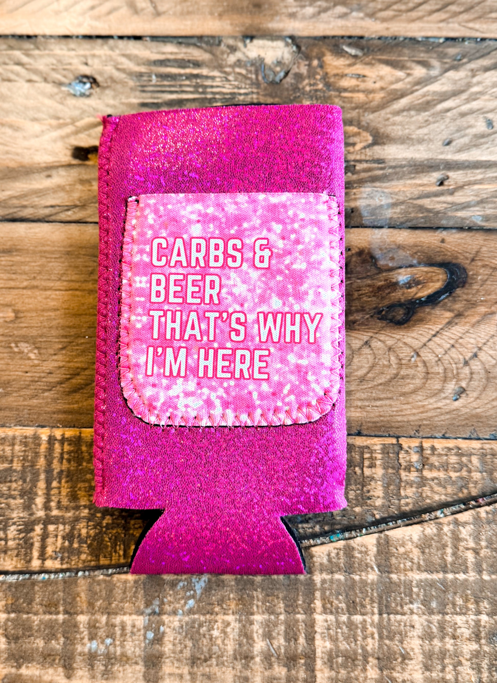 Hot pink glitter slim can cooler with a light pink patch that says “CARBS & BEER THAT’S WHY I’M HERE” in white outlined text.