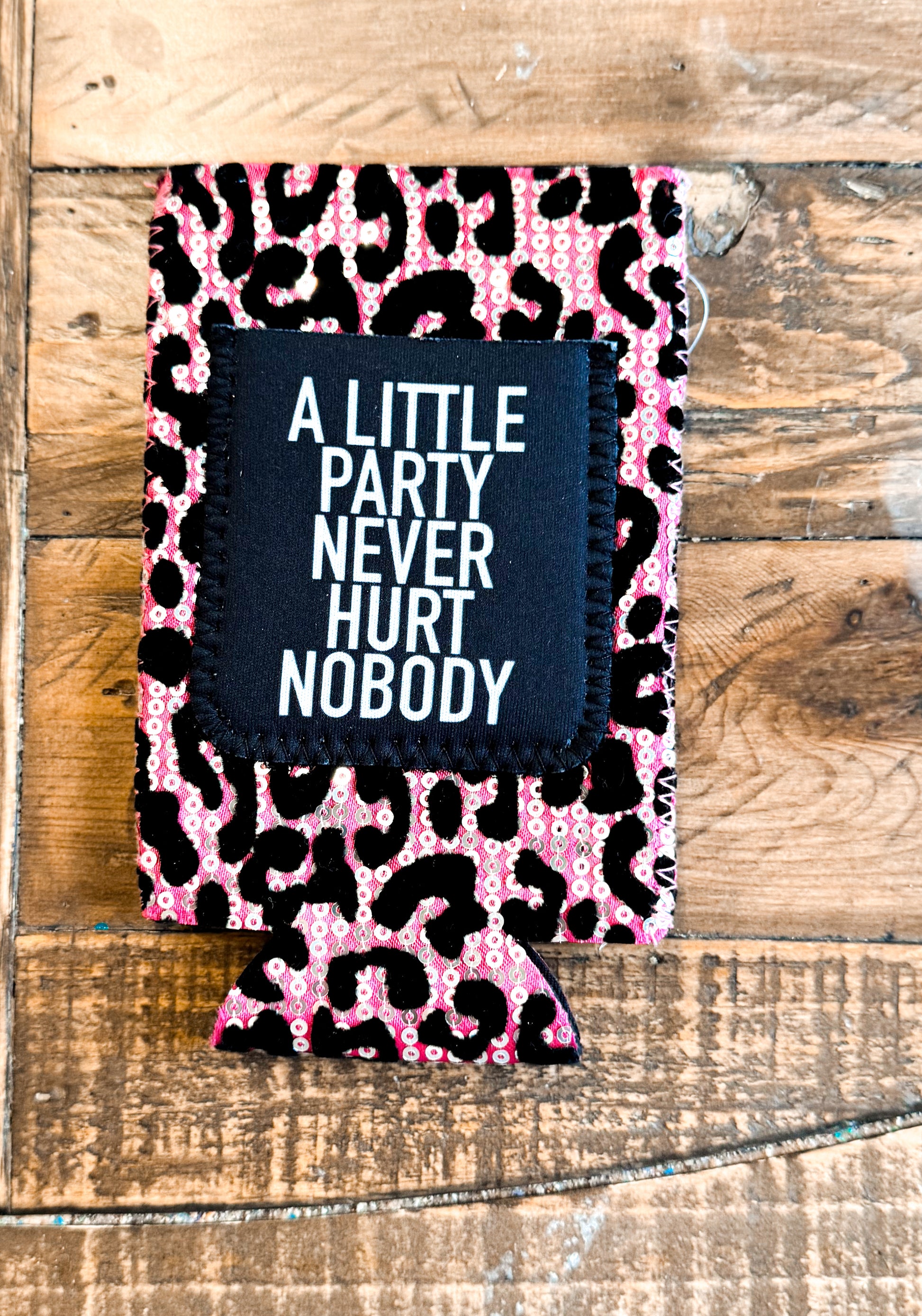 Pink leopard sequin slim can cooler with a black patch that says “A LITTLE PARTY NEVER HURT NOBODY” in bold white text.