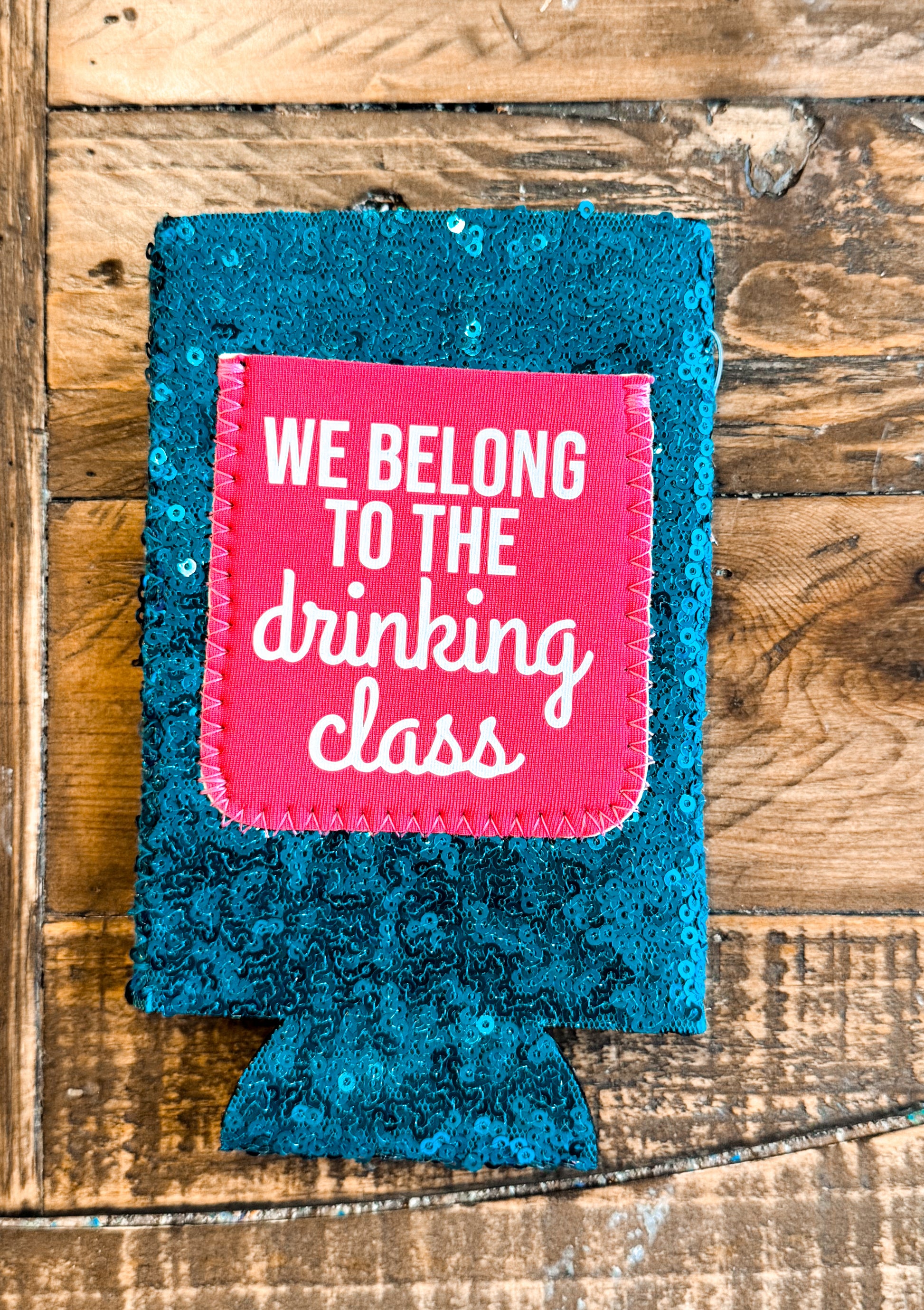Teal sequin slim can cooler with a hot pink patch that reads “WE BELONG TO THE DRINKING CLASS” in playful white font.