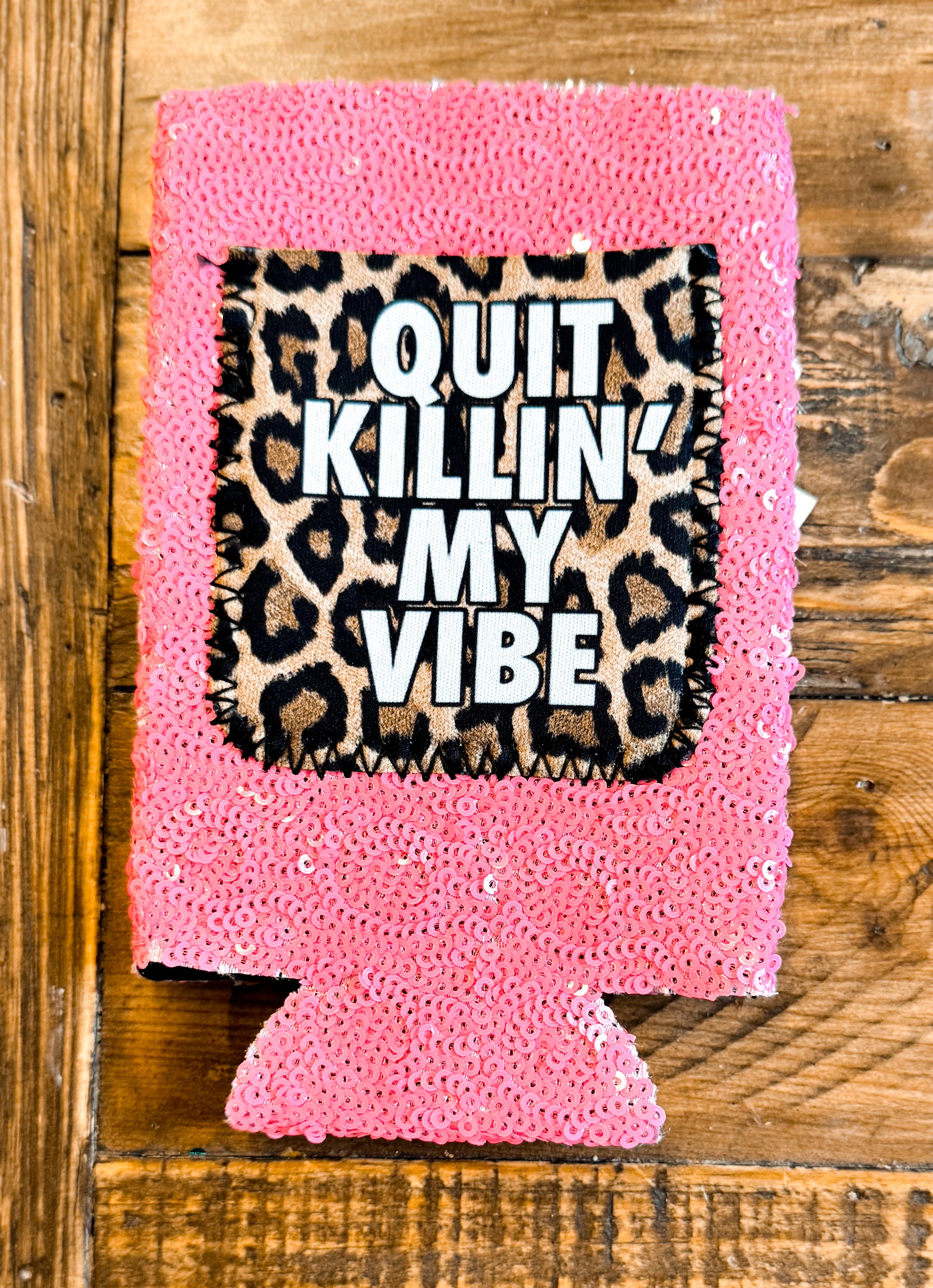 Pink sequin slim can cooler with a leopard print patch that says “QUIT KILLIN’ MY VIBE” in bold white letters.