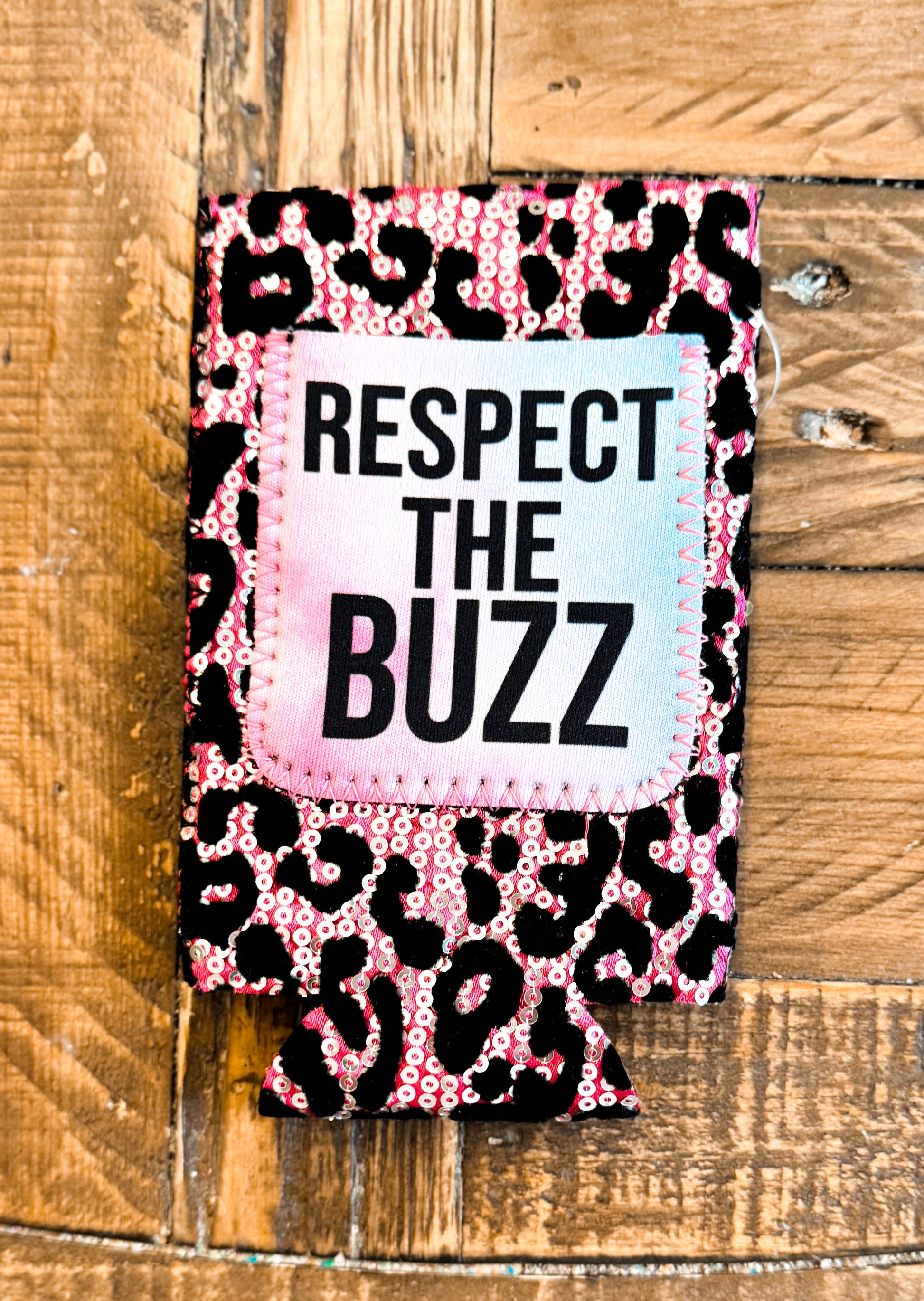 Pink leopard sequin slim can cooler with a pastel tie-dye patch that says “RESPECT THE BUZZ” in bold black font.