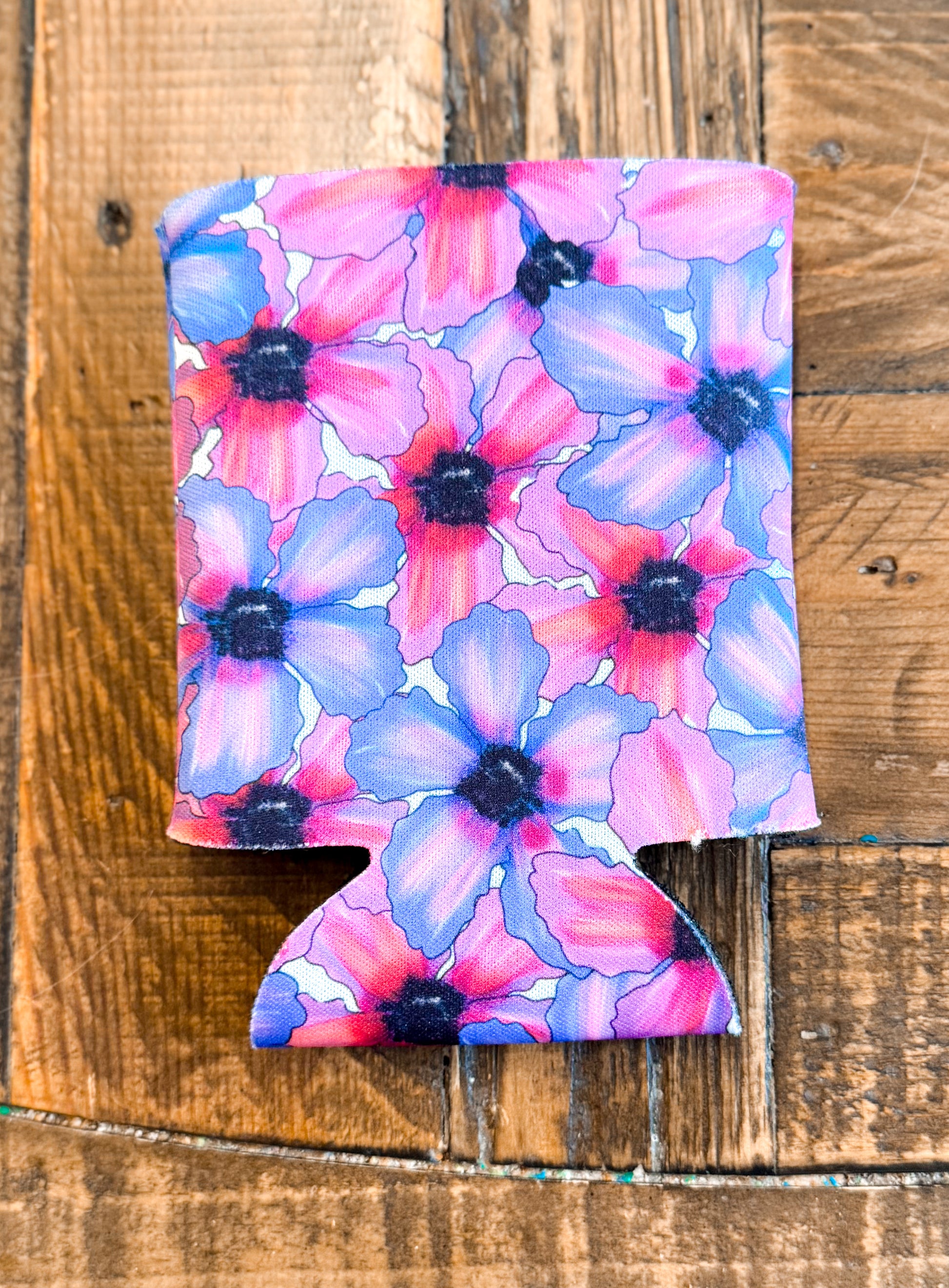 Colorful floral can cooler featuring a bold pattern of red, purple, and blue watercolor-style flowers with dark centers, set against a rustic wood background.