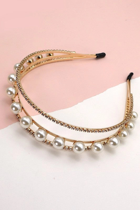 Gold double-band headband featuring large pearls and rows of rhinestones, styled on a pastel surface next to a wooden box. Elegant, feminine, and glam accessory.