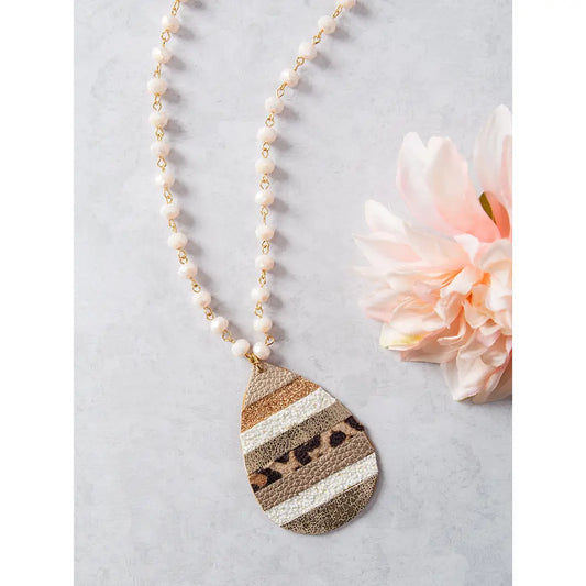 Teardrop-shaped pendant necklace with glittery stripes and leopard print on a beaded chain, styled with a blush pink flower on a light background.