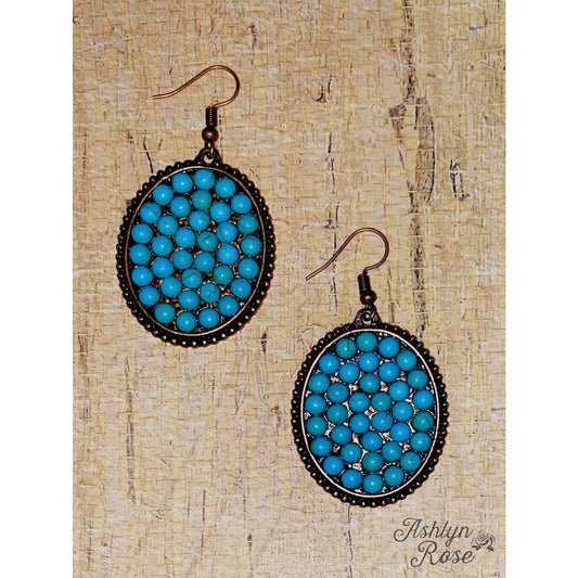 Pair of oval dangle earrings with turquoise beads set in antique bronze frames, displayed on a textured wood background with "Ashlyn Rose" watermark.
