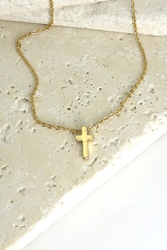 Gold-dipped cross necklace with a delicate chain, featuring a small, polished vertical cross pendant resting on a textured stone background.