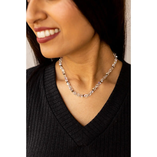 Woman wearing the Moonlit Mirage Necklace — a delicate strand of clear faceted beads with gold accents — styled with a black ribbed V-neck top.