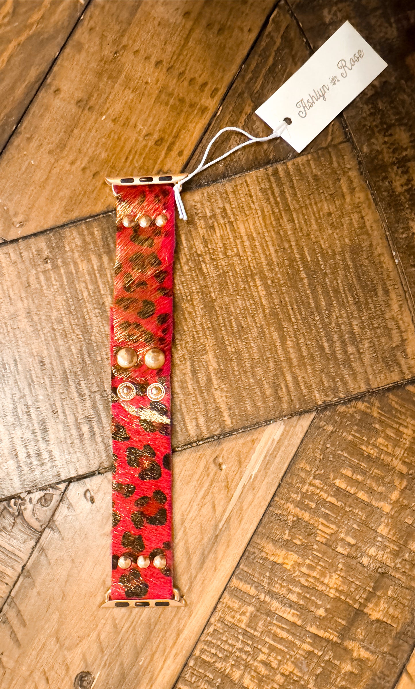 Vibrant pink and gold leopard print Apple Watch band with faux fur texture and gold snap accents, styled on rustic wood surface.