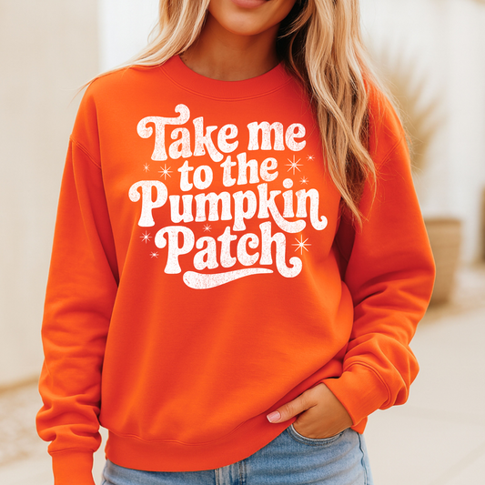 woman wearing a burnt orange crewneck sweatshirt with the phrase “Take me to the Pumpkin Patch” printed in bold white retro-style lettering. The sweatshirt has a relaxed fit, and the woman is standing outdoors with one hand in her pocket.